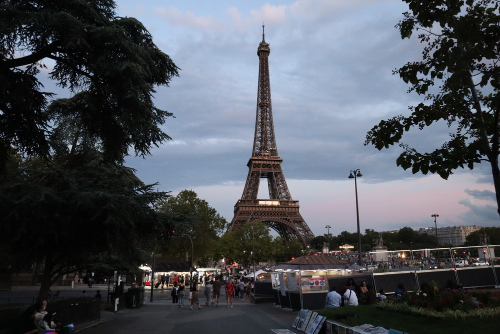 A crowd gathers in front of the Eiffel tower at dusk.